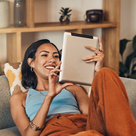 Woman smiling while looking at tablet on couch