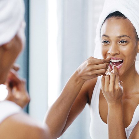 Woman smiling while flossing teeth in bathroom