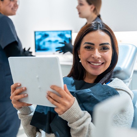 Patient smiling while holding mirror in treatment chair