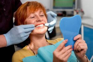 Woman with implants looking into mirror in dentist's chair. 