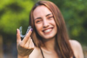 Woman holding up Invisalign clear aligner. 